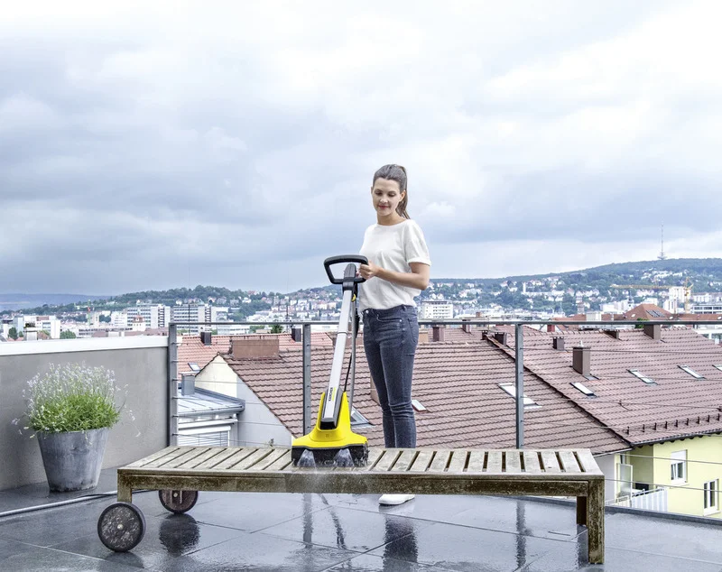 Person steht auf einer Terrasse und hält einen Kärcher Bodenreiniger. Im Hintergrund sind Dächer und eine Stadtlandschaft zu sehen.