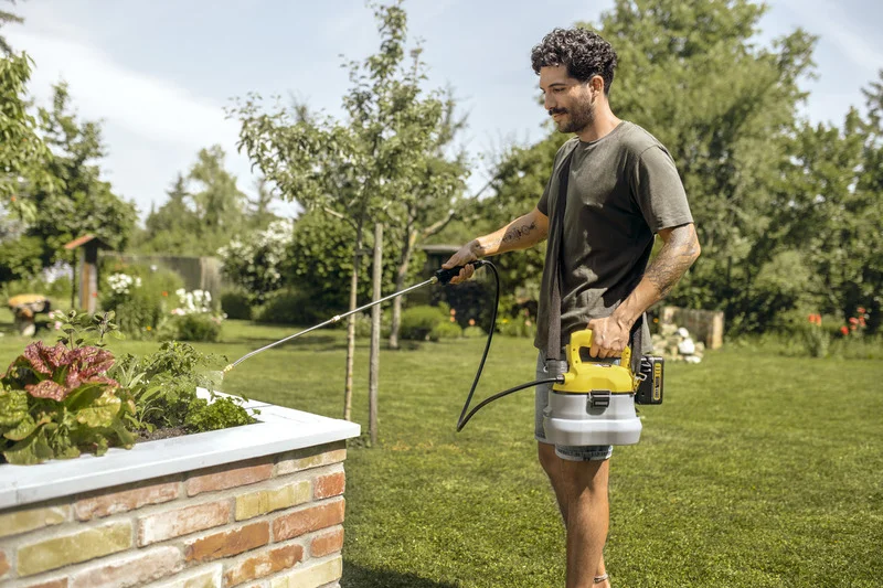 Mann in einem Garten nutzt einen Kärcher Hochdruckreiniger, um Pflanzen in einem gemauerten Hochbeet zu bewässern.