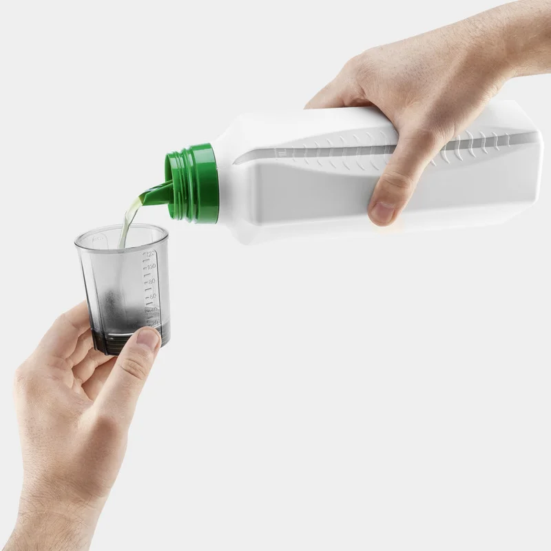 Hand hält weiße Flasche mit grünem Deckel, gießt Flüssigkeit in transparenten Messbecher.