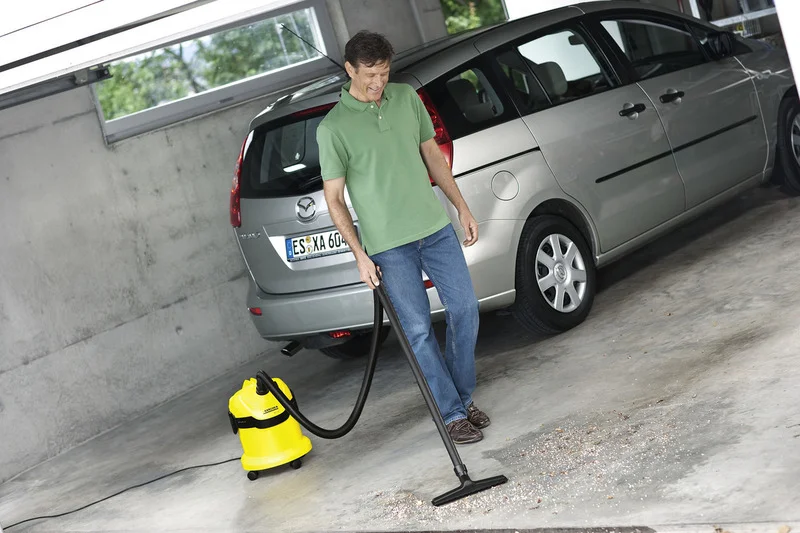Mann reinigt Garageboden mit einem gelben Kärcher Nass-Trockensauger neben einem silbernen Mazda.