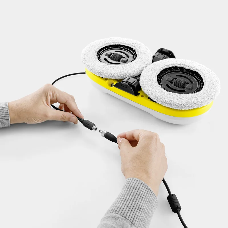 Hände verbinden Kabel mit Kärcher Bodenreiniger, gelb mit zwei weißen Reinigungspads, auf weißem Hintergrund.