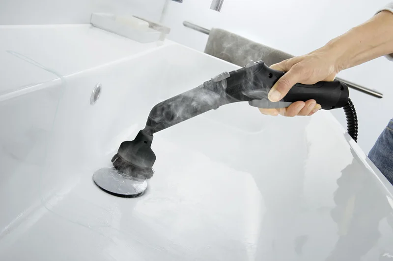 Hand hält Kärcher Dampfreiniger, reinigt weißen Waschbeckenabfluss. Dampf steigt auf, Badezimmerumgebung sichtbar.