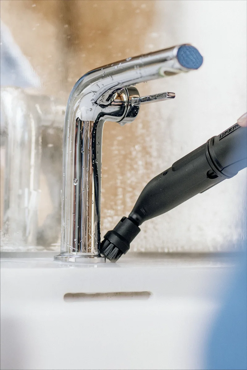 Kärcher Reinigungsgerät mit Bürstenaufsatz reinigt Wasserhahn.