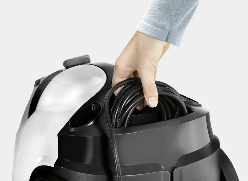 Hand legt Kabel in Kärcher Hochdruckreiniger. Gerät ist schwarz-weiß, Nahaufnahme. Hintergrund neutral grau.