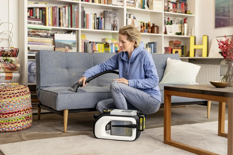 Person reinigt graues Sofa mit Kärcher Waschsauger in einem Wohnzimmer mit Bücherregal und Dekorationen.