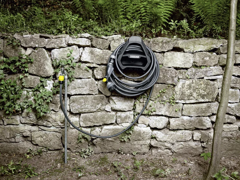 Gartenschlauch an einer Steinmauer befestigt, mit einem Kärcher Schlauchhalter und Wasserhahn mit gelbem Anschluss.