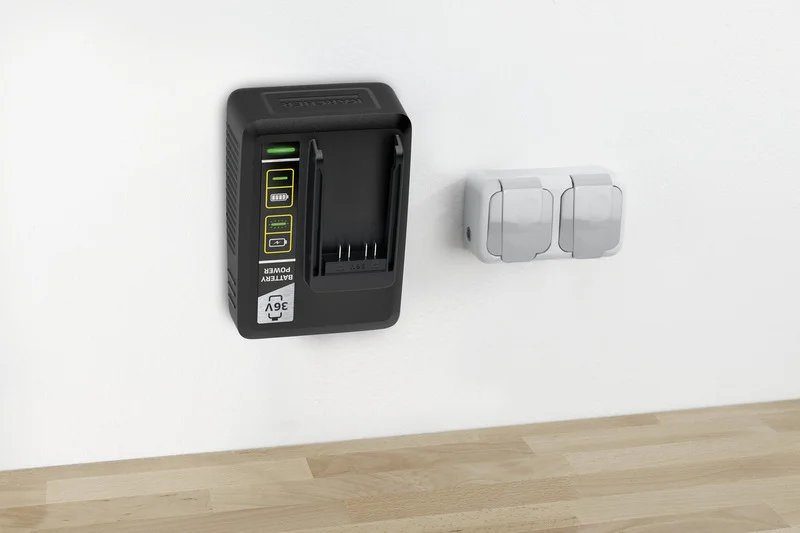 Kärcher Batterieladegerät an weißer Wand montiert, daneben zwei graue Steckdosen, darunter Holzoberfläche.