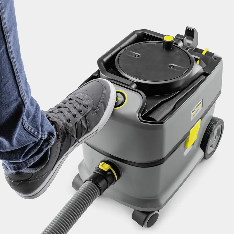 Fuß drückt auf den Einschaltknopf eines Kärcher Nass-/Trockensaugers. Graue Hose und Turnschuhe sichtbar.