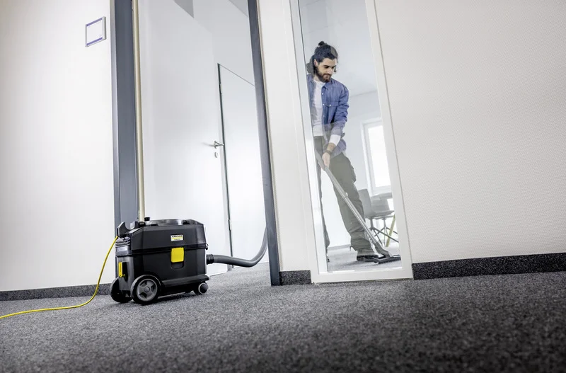 Person reinigt Teppichboden mit Kärcher Nass-/Trockensauger in einem Büro. Der Sauger steht im Vordergrund, die Person im Hintergrund.