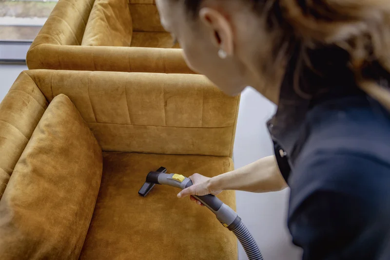 Person reinigt braunes Sofa mit einem Kärcher Staubsauger in einem Innenraum.