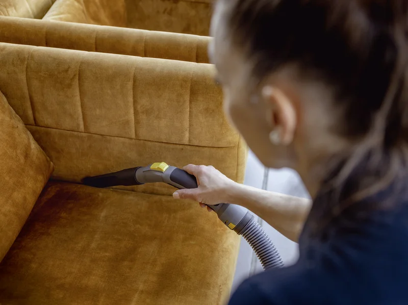 Person reinigt braunes Sofa mit Kärcher Staubsauger in einem Innenraum.