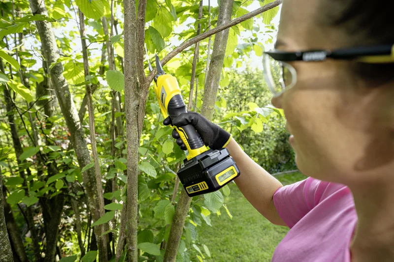 Person schneidet mit einem Kärcher Astschere einen Ast im Garten. Sie trägt schwarze Handschuhe und ein rosa T-Shirt.