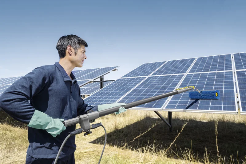 Person reinigt Solarpanel mit Kärcher Reinigungsgerät im Freien. Klarer Himmel, trockene Grasfläche im Hintergrund.