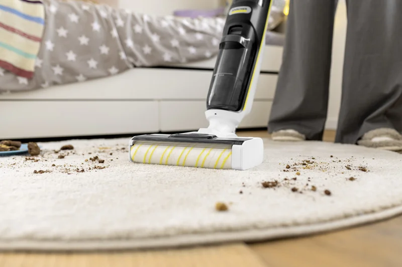 Kärcher Bodenreiniger reinigt Teppich in einem Schlafzimmer, umgeben von Krümeln und Schmutz. Person steht daneben.
