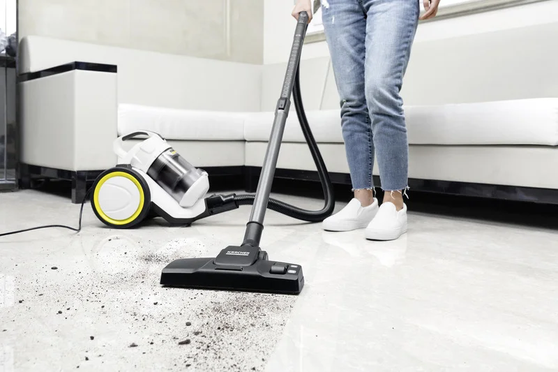 Person mit Jeans und weißen Schuhen saugt Schmutz vom Boden mit einem Kärcher Staubsauger in einem modernen Wohnzimmer.
