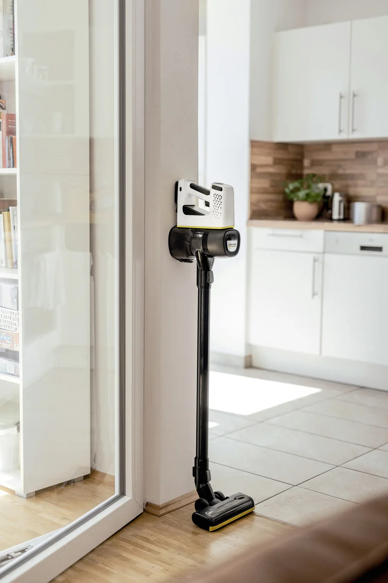 Kärcher Akku-Staubsauger steht in einer modernen Küche an der Wand, mit Holzboden und weißen Schränken.