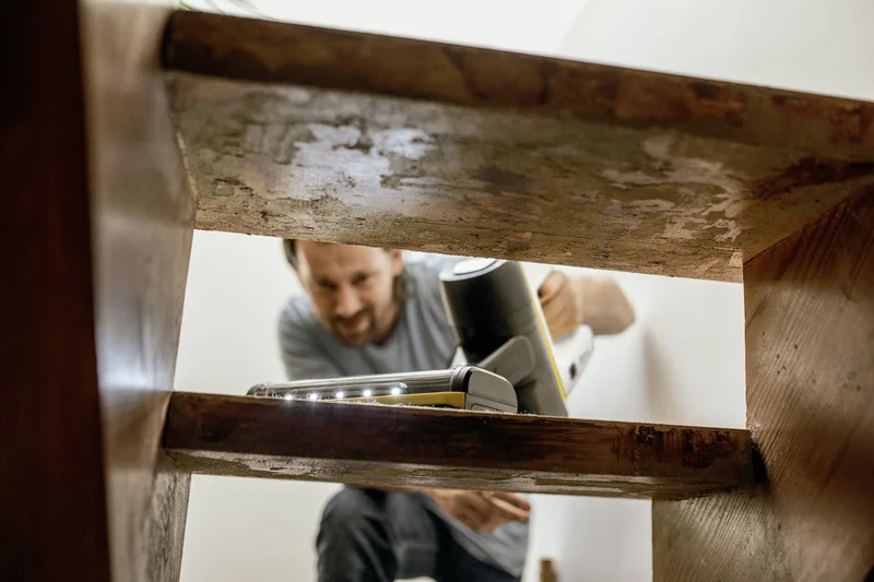 Person reinigt Holztreppe mit einem Kärcher Fenstersauger in einem Innenraum. Sicht von unten auf die Treppe.