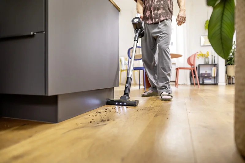 Person reinigt Holzboden mit einem Kärcher Akku-Staubsauger in einem Wohnzimmer. Möbel und Pflanzen im Hintergrund.