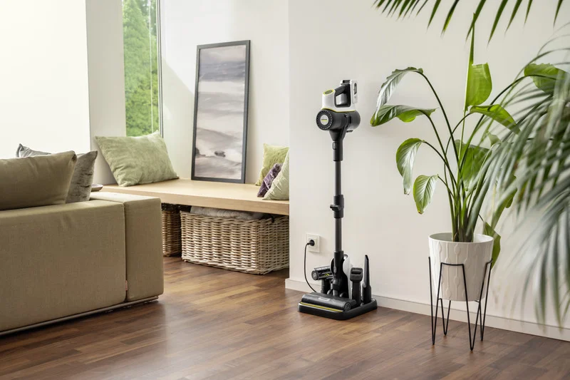 Kärcher Akku-Staubsauger steht in einem modernen Wohnzimmer mit Holzboden, neben einem großen grünen Pflanzen und einem Sofa.