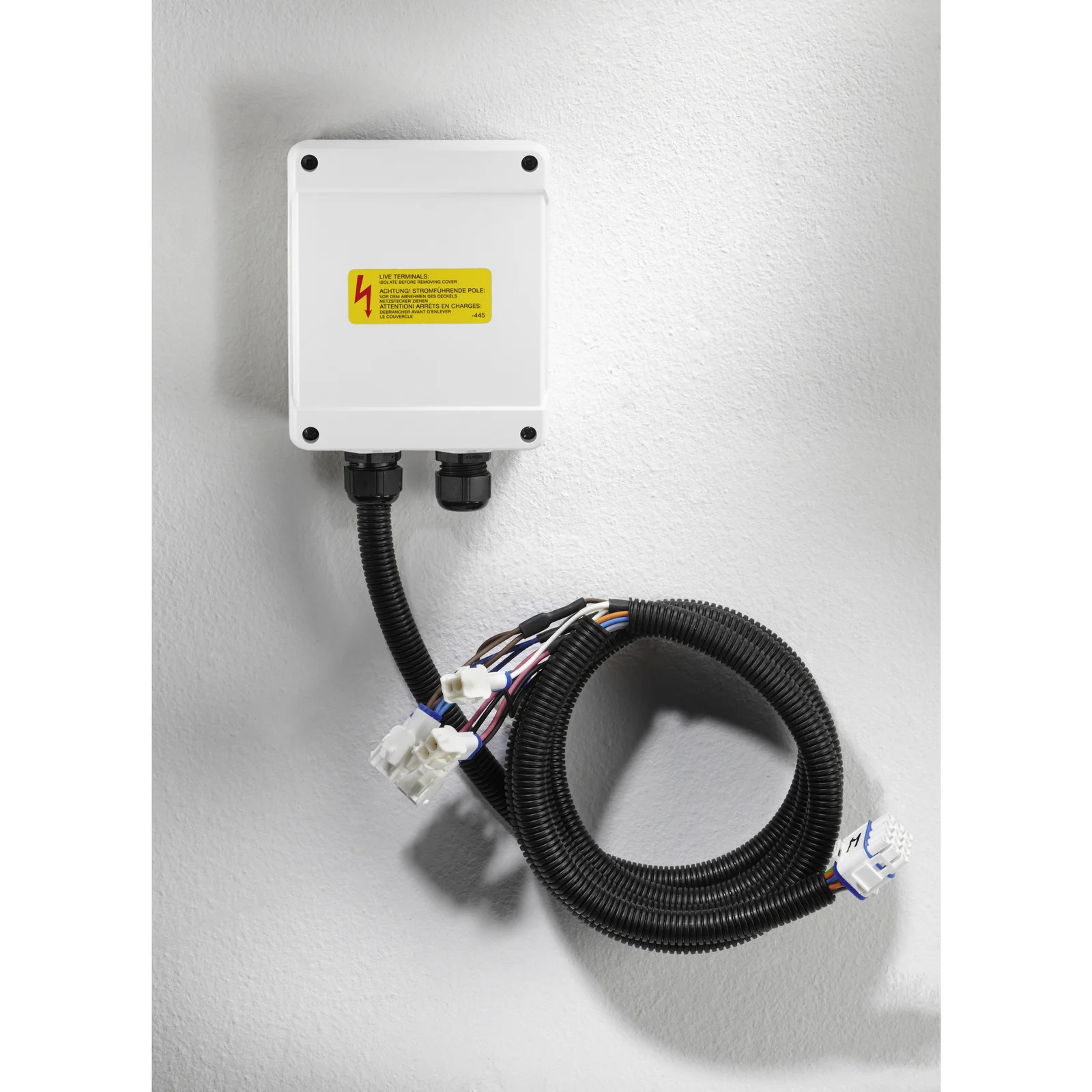 Weiße elektrische Anschlussdose mit gelbem Warnhinweis, zwei Kabelanschlüssen und schwarzem Kabelstrang an einer Wand.