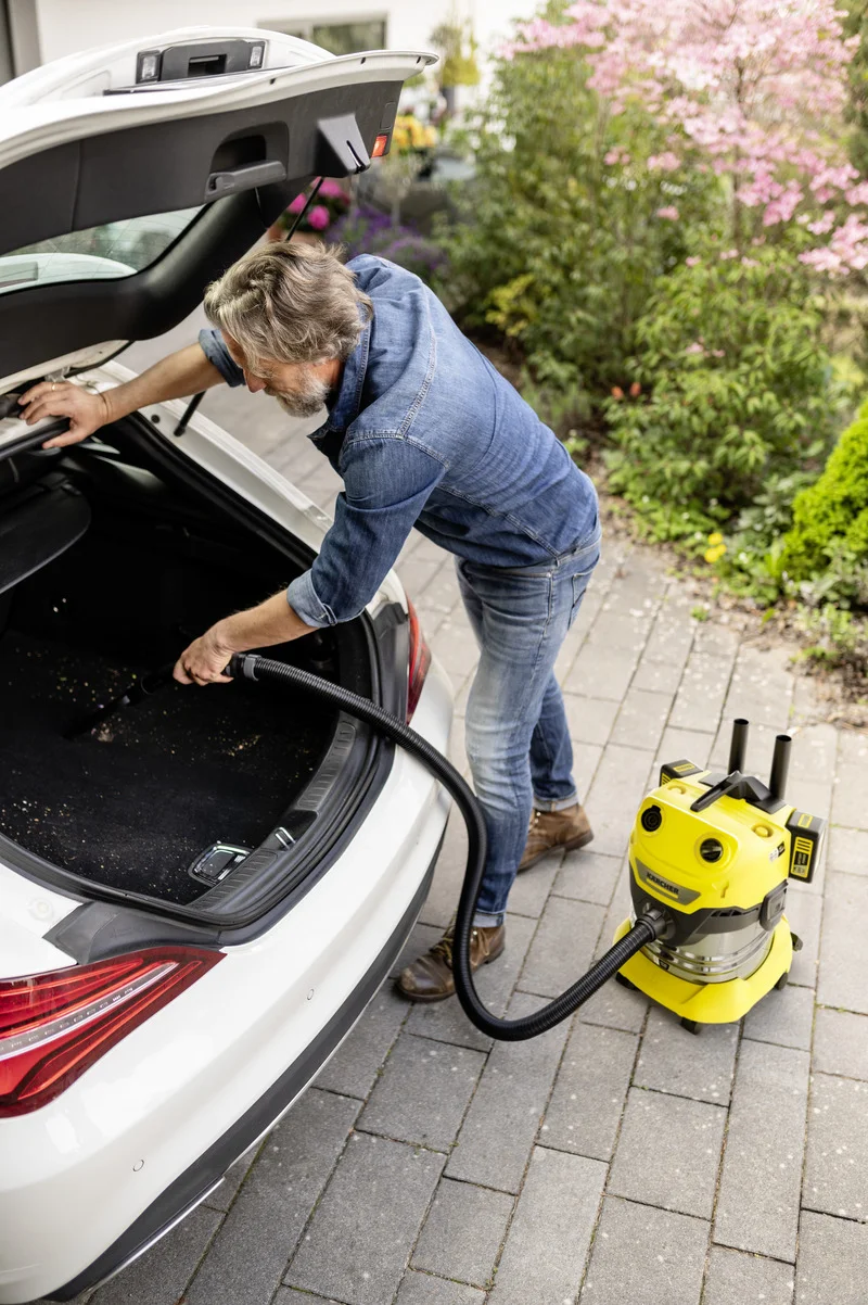 Mann reinigt Kofferraum eines weißen Autos mit einem Kärcher Nass-Trockensauger im Freien.
