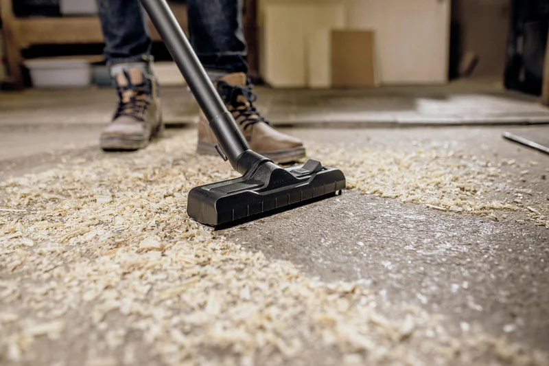 Kärcher Staubsauger saugt Holzspäne auf Werkstattboden, Person in Arbeitsschuhen im Hintergrund.