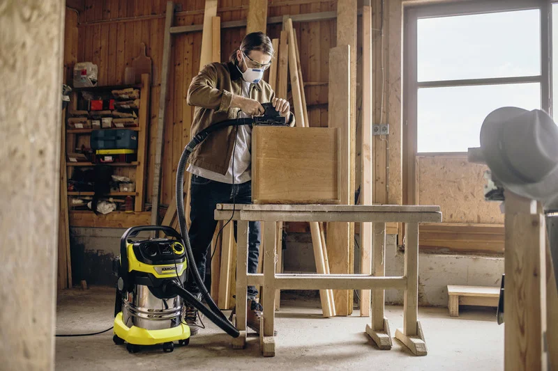 Person arbeitet in Werkstatt mit Kärcher Nass-Trockensauger, Holzwerkbank und Holzbrettern im Hintergrund.
