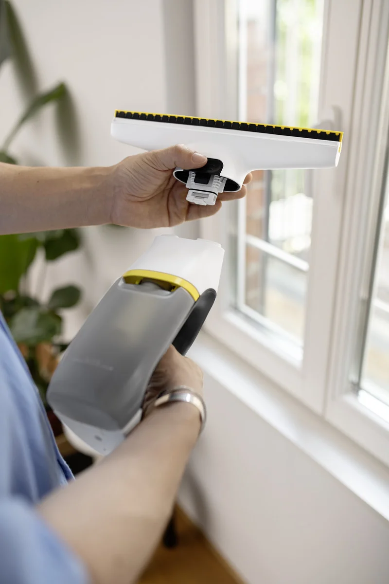 Person hält Kärcher Fenstersauger vor einem Fenster. Im Hintergrund sind Pflanzen zu sehen.
