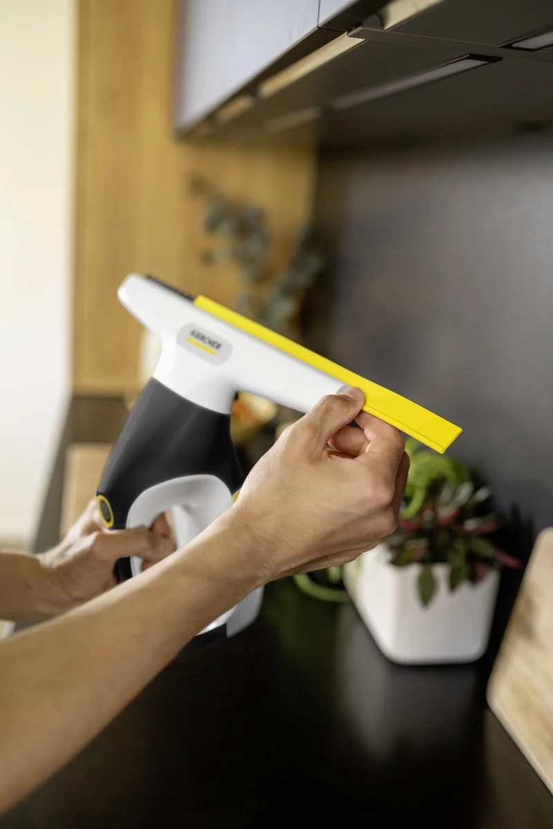 Person hält Kärcher Fenstersauger in der Hand, im Hintergrund Pflanze auf schwarzer Arbeitsplatte.