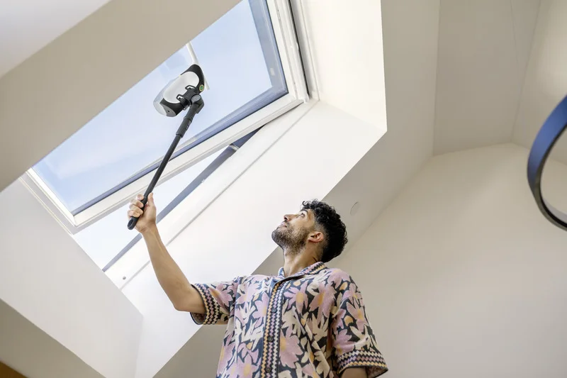 Mann reinigt Dachfenster mit einem Kärcher Fensterreiniger in einem hellen Raum.
