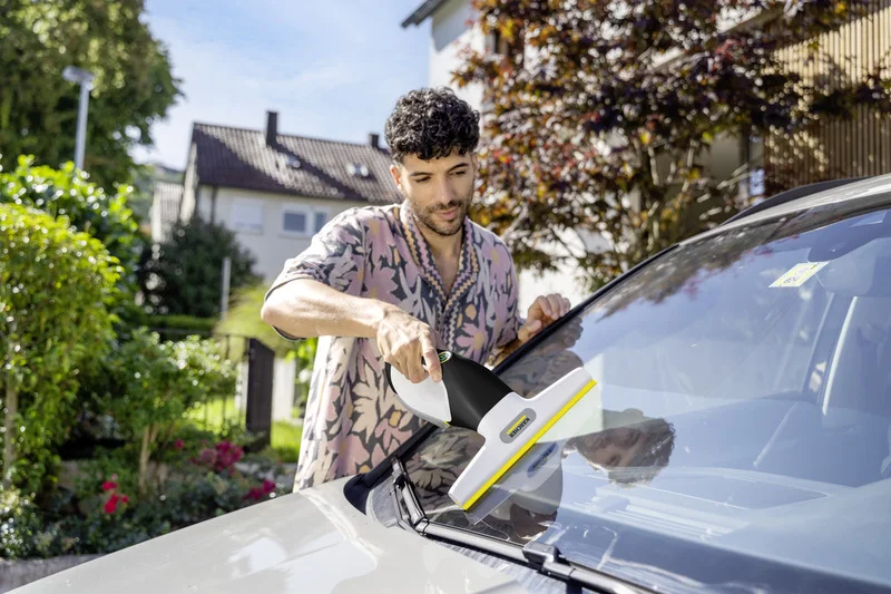 Person reinigt Autoscheibe mit Kärcher Fenstersauger im Garten.