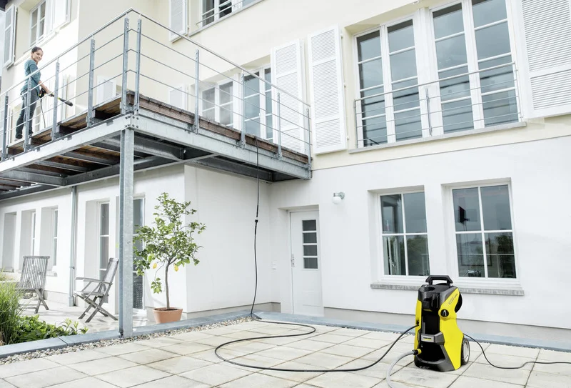 Kärcher Hochdruckreiniger auf einer Terrasse vor einem modernen Gebäude, Person reinigt Geländer auf dem Balkon.