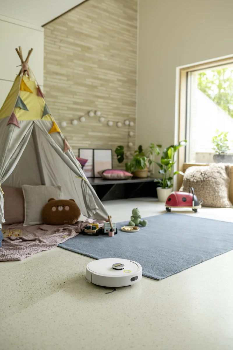 Wohnzimmer mit Spielzelt, Spielzeug und Pflanzen. Ein weißer Kärcher Saugroboter auf dem Boden.