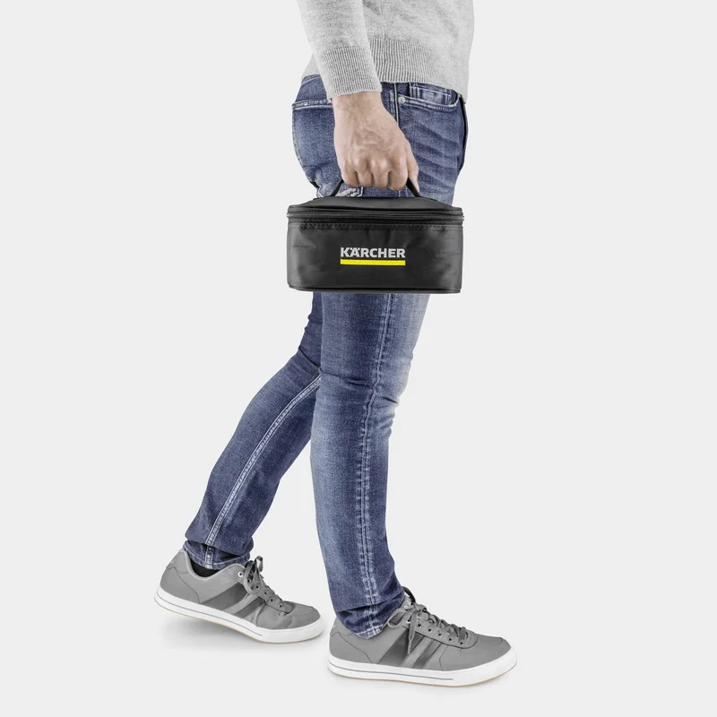 Person in Jeans und grauem Pullover trägt eine schwarze Kärcher Tasche mit gelbem Logo. Graue Sneakers auf hellem Hintergrund.