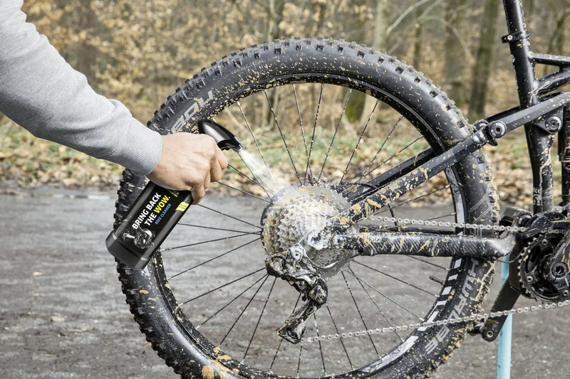 Hand sprüht Fahrradreiniger auf schmutziges Mountainbike-Rad im Freien. Fahrradkette und Ritzel werden gereinigt.