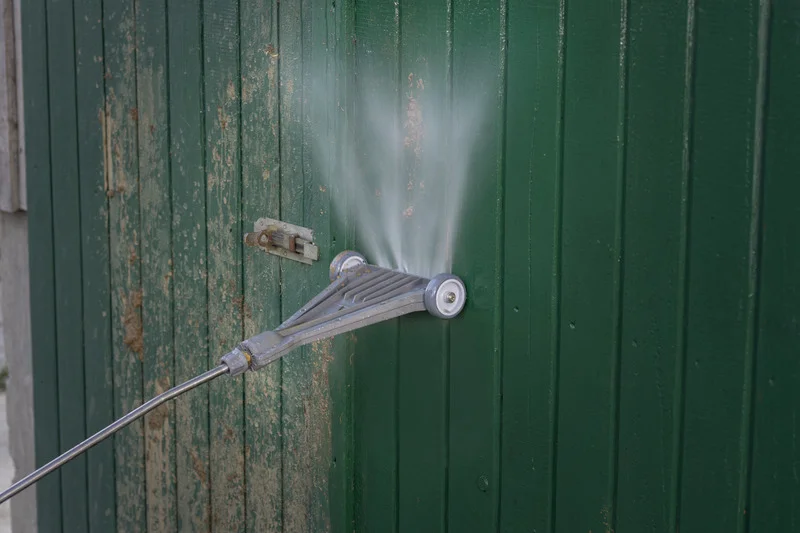 Kärcher Hochdruckreiniger sprüht Wasser auf eine grüne Holzwand im Freien.